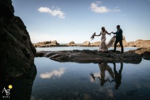   A reflection in the tidal pools at Tunnels Beaches, UK, delivers a unique and artistic perspective as the couple walks, merging landscape and romance.