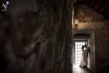   Inside Malcesine Castle on Lake Garda, Italy, the couple is silhouetted in a tender embrace near a barred window, soft shadows from the ancient stone walls creating a romantic scene.