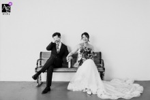   At the groom's home in Singapore, the couple sits together on a bench, sharing a lighthearted portrait as the groom laughs with visible joy.