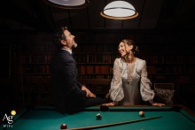 Couple Shares Private Smile By Pool Table Lit At Château De Denonville France Sharing a private smile, the couple stands by the pool table at Château de Denonville, France, their faces lit only by the table’s lights, creating an intimate and stylish portrait.