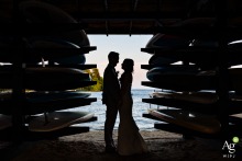 The bride and groom are silhouetted between paddleboards at Camp Mataponi in Maine, their figures outlined against the light on their adventurous wedding day.