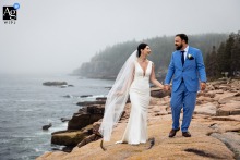   The bride and groom traverse the dramatic cliffs of Acadia National Park in Maine on their wedding day, the sweeping landscape providing a breathtaking backdrop to their walk together.