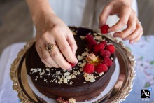 Fresh Raspberries Top The Wedding Torte At Pine Lake Beach House In Pine Lake, Georgia At Pine Lake Beach House in Pine Lake, Georgia, the bride carefully arranges fresh raspberries on a gluten-free chocolate torte, capturing a thoughtful wedding-day detail before the celebration begins.