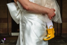 On the steps of Chester Town Hall in Cheshire, UK, a woman in a white wedding dress holds a child wearing bright yellow wellington boots, creating a charming close-up that contrasts timeless bridal elegance with playful childhood color.