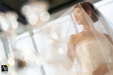 At the Grand Hyatt Shanghai, China, the bride is photographed through the soft focus of a wine glass, bathed in warm light as she enjoys a quiet portrait during her wedding preparations.