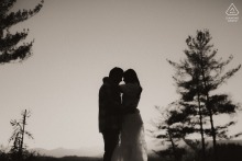 At Lake James in Nebo, NC, a couple's silhouette is beautifully framed by a few trees, set against the vibrant hues of a sunset, capturing a serene and romantic scene.