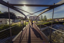 A couple stands and poses on a steel structure footbridge in Piazza 4 Novembre, Ceparana, exuding romance and adventure.