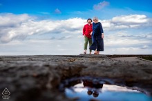 A couple poses at Rattray Marsh, their reflection visible in a clear puddle.