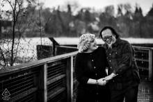 A couple at Rattray Marsh laughs joyfully, captured in a black and white portrait, surrounded by nature's tranquil beauty.
