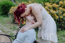 A couple shares a tender kiss on a bench at Gellért-hegy, framed by scenic views and vibrant nature.