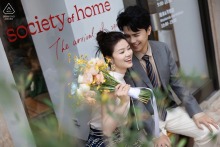 Engaged couple walks along the Bund, Shanghai, smiling and posing with bouquet before Society of Home.