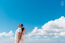In Joinville, Santa Catarina, a couple stands back to back, smiling at the sky. The minimalist composition features blue skies and clouds, expertly captured by a talented WPJA photographer.