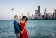 A seagull flies above a couple on a windy engagement session at Chicago’s North Avenue Beach.