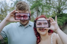 Playful couple at Gellért-hegy use smartphones showing their faces, creating a quirky, humorous illusion.