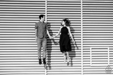 Engaged couple joyfully leaps outside Kennedy Center, Washington DC, capturing excitement in modern architectural setting.