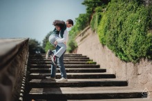Playful engaged couple smiles and laughs on stone steps at Fortezza Medicea, Siena, Tuscany, Italy.
