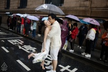 Couple poses for a portrait on rainy Shanghai Bund street, surrounded by onlookers holding colorful umbrellas.