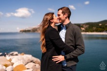 Engaged couple kissing in the wind, sunny day, by the sea, Portopiccolo, Sistiana, Trieste, Italy.