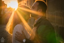 Engaged couple poses in afternoon light, sun rays crossing before them, Baeza, Jaén, Spain setting.