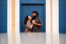 A couple embraces in a symmetrical portrait in Maceió, Brazil, with visible soft reflections.