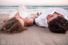 An engaged couple smiles widely, embracing on the sand in Maragogi, Alagoas, by the sea.