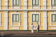 Engaged Couple Holding Hands Before Historic Yellow And White Building In Bangkok, Thailand Bangkok, Thailand. Couple holding hands with an old yellow and white building as their backdrop.