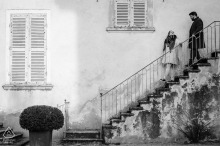 Charly, France: Vintage Engagement Elegance Descends a Grand Staircase CHARLY, France — A couple descends a grand staircase in an old public park. This vintage-style, black-and-white portrait captures their classic elegance during an engagement shoot.