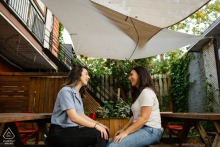 Montreal Engaged Couple Shares A Warm, Intimate Gaze Under A Shady Canopy MONTREAL, Quebec — An engaged couple shares a warm and intimate gaze while seated at a picnic table under a shady canopy, a tender scene captured during their portrait session.