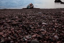 An engaged couple embraces by the rocky Duluth, MN lakeside, Lake Superior visible behind them.