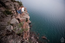 An engaged couple dances joyfully on the edge of a cliff in Duluth, MN, overlooking Lake Superior.