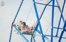 Couple snuggles closely together on a Ferris wheel at The Fun Zone, Newport Beach, California, during their engagement shoot.