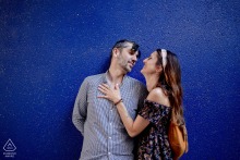 In Paris, France, a couple stands with their backs to a minimalist painted blue wall. She gently places her hand on his chest, capturing a quiet, intimate connection in their urban engagement portrait.