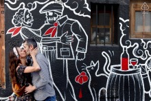 In Paris, France, a couple poses in front of striking street art featuring white line drawings on a black background, accented with vivid red highlights, blending romance with urban creativity in their engagement portrait.