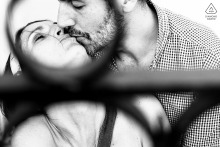 In Paris, France, a couple shares a kiss framed by the circular design of an iron fence. The black and white portrait highlights the romance and timeless charm of the city.