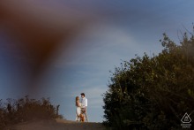 At Point Dume Natural Preserve in Malibu, California, a couple poses with their dog for an engagement photo. Big bushes frame each side, and a blue sky stretches overhead, creating a picturesque scene.