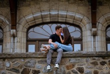 Newly Engaged Couple Shares Tender Moment On Mount Royal Chalet Balcony Edge At Mount Royal Chalet in Montreal, QC, Canada, a newly engaged couple relaxes together on the edge of the balcony, their foreheads touching gently.