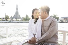 Bangkok Boardwalk Bliss: Hand-in-Hand, Our Love Story by the Water Couple portrait from Bangkok, Thailand, showing the pair seated close together on a boardwalk bench, holding hands with the water visible right behind them.