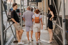 NYC engagement photography: Candid portrait in Central Park under scaffolding. Couple is the focus, with pedestrians adding a dynamic urban background.