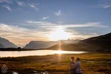 An engaged couple shares a candid embrace by the water at Lac du Pontet, France. The image captures the golden light of sunset, highlighting their quiet connection at day's end.