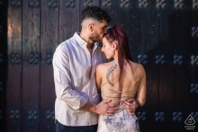 A pre-wedding couple is standing side-by-side in Baeza, Spain. The male subject faces the camera, while the female subject's back is toward the lens, creating a contrasting view of their parallel stance. 