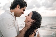 An engaged couple shares passionate gazes at sunrise on Praia de Ipioca, Brazil. The soft, warm light of dawn illuminates their faces, emphasizing the depth of their affection on the beach.