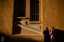 This beautiful sunrise summer portrait in Aix-en-Provence captures the couple standing side-by-side against a warm-toned stucco building, framed dramatically by long shadows.