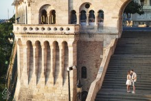 In Budapest's golden light, the couple stands on the massive stairs of an old world stone castle, a stunning portrait that captures their love and the city's majesty.