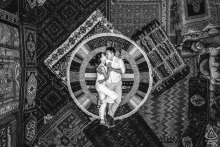 In Göreme, Nevşehir, Turkey, a Cappadocia pre-wedding drone shot captures the couple lying on rugs inside a carpet vendor, facing each other amidst intricate patterns.