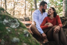 Engaged Couple Portrait Among Moss Covered Boulders in Lac Chambon Forest At Lac Chambon in France, the couple sits close together among moss-covered boulders in a lush forest, surrounded by the serene natural beauty.