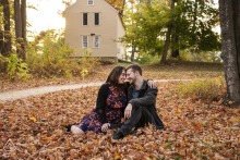 At Minuteman National Park in Concord, Massachusetts, a couple sits together in autumn leaves, center framed with their foreheads touching for a portrait.