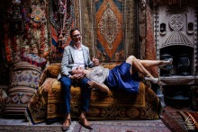 An engaged couple poses on a couch inside a carpet vendor’s shop during a pre-wedding photo session in Cappadocia, Göreme, Nevşehir, Turkey, with natural light streaming from above.