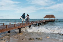 Couple playfully runs away from the approaching waves on a low wooden pier at Viceroy Mexico Riviera Maya, their laughter and energy set against the ocean’s lively backdrop.