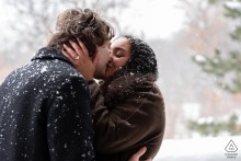 Newly engaged couple passionately embracing at Kondiaronk Belvedere in Montreal, Quebec, framed by gently falling snow, their warmth and affection contrasting with the wintry city backdrop.
