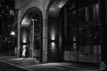 Couple stands together on a city sidewalk at night in the City of London, captured in a black and white portrait that highlights the urban lights and nighttime atmosphere surrounding them.